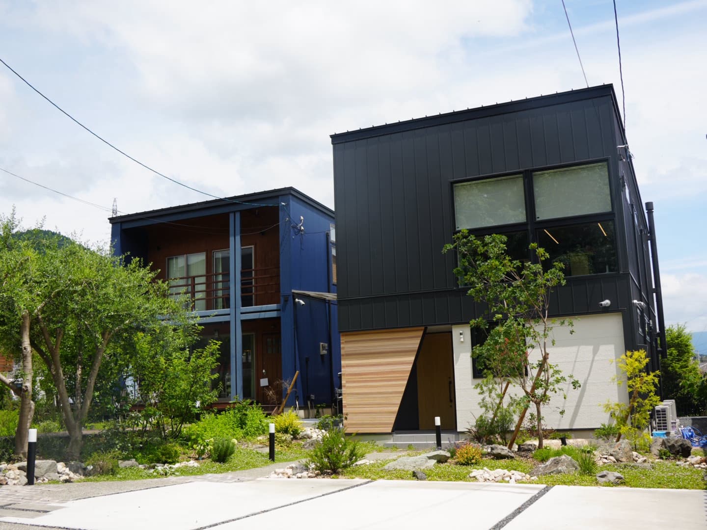 事業所の外観。青と黒の2棟が並ぶモダンな建物と、緑豊かな庭。